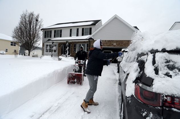 Um homem tira a neve do chão enquanto outro faz o mesmo, só que no carro, em West Seneca