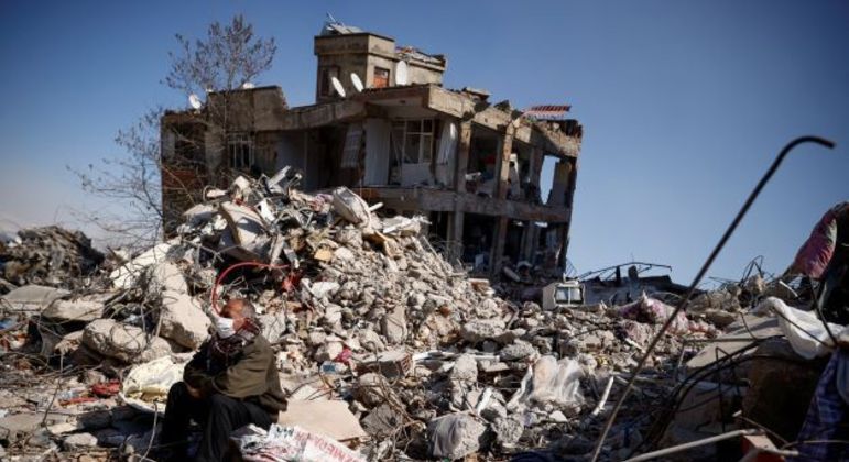 Homem sentado em meio a destroços de terremoto em Kahramanmaras