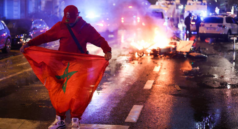 Torcedor segura a bandeira do Marrocos em meio a tumulto em Bruxelas após a vitória africana sobre a Bélgica na Copa
