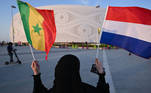 Torcedora carrega as bandeiras de Senegal e Holanda na porta do Al Thumama Stadium, em Doha