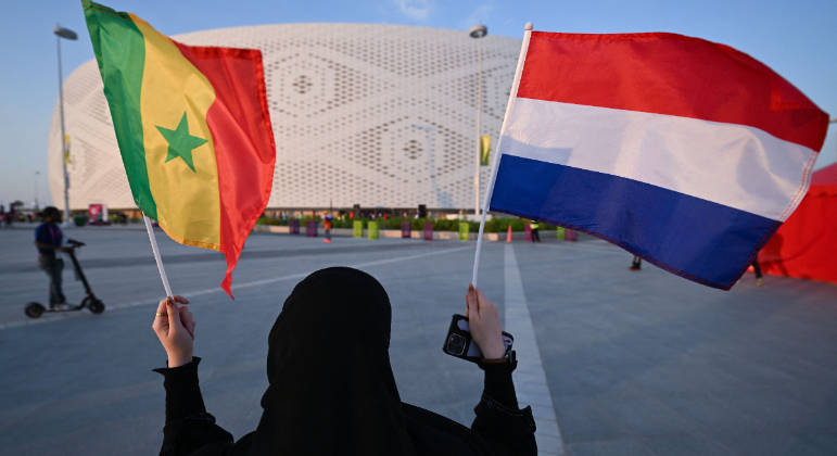 Torcedora carrega as bandeiras de Senegal e Holanda na porta do Al Thumama Stadium, em Doha