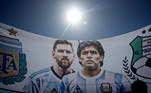 Certamente, eles não iriam faltar! Torcedores colocam Messi e Maradona lado a lado em bandeiras e exaltam os craques campeões mundiais da Argentina