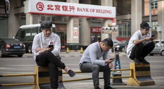 Três homens em rua na China olhando para seus celulares
