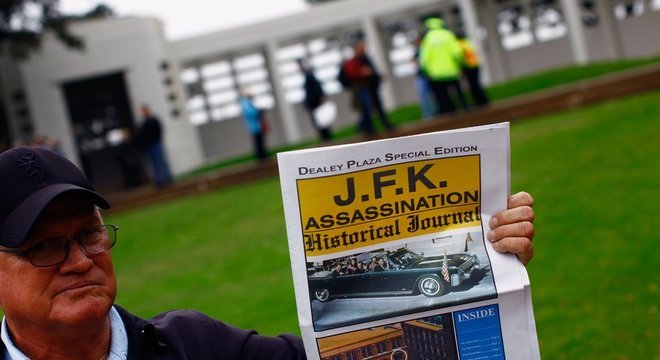 Turista segura jornal falando da morte de John Kennedy em frente à praça Dallas, nos EUA