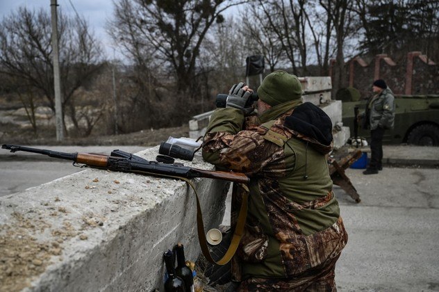 Um soldado ucraniano olha através de binóculos para a cidade de Stoyanka, na Ucrânia, em um posto de controle antes da última ponte na estrada que liga Stoyanka a Kiev