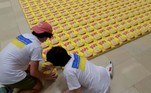 As caixas de cereal — amarelas e azuis — foram doadas por uma empresa de alimentos. Ao todo, o mosaico ocupa um espaço de cerca de 266 m². Os jovens passaram diversas horas da última quinta-feira (11) construindo a obra