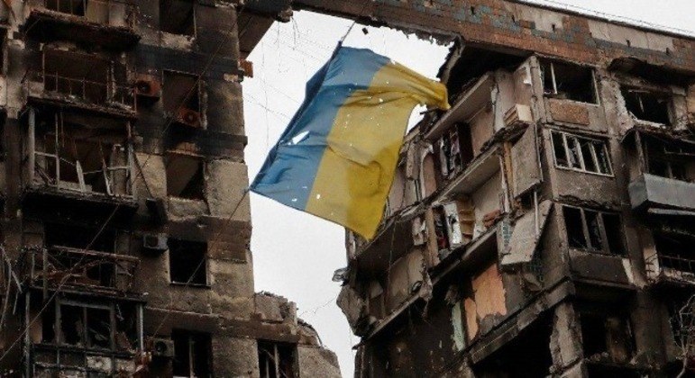 Bandeira da Ucrânia é vista pendurada em frente a um prédio destruído no país