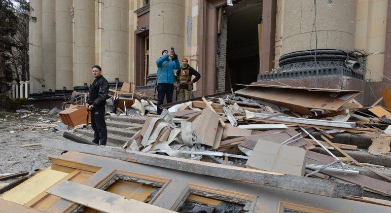 Homens ficam do lado de fora da prefeitura de Kharkiv, destruída após bombardeio russo