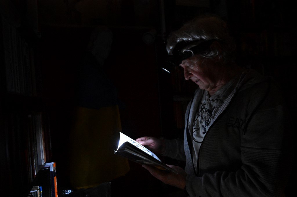 Igor Zhuk, de 70 anos, lê um livro com a ajuda de uma lanterna, em Kiev 
