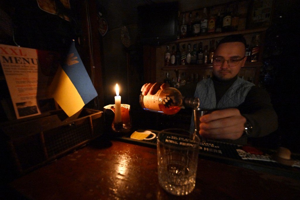 Homem serve uma bebida à luz de velas durante um corte de energia em Kiev