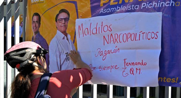 Uma ciclista pendura um cartaz contra a violência do narcotráfico nas grades de um complexo esportivo em Quito