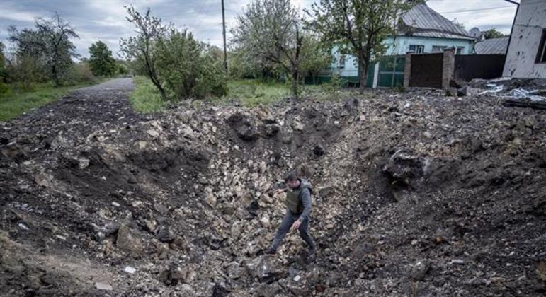 Homem examina cratera de explosão no centro da vila de Slatino, na região de Kharkiv, Ucrânia