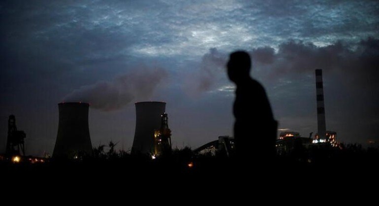 Um homem passando em frente a uma termelétrica movida a carvão em Xangai, na China