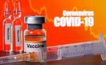 FOTO DA ILE: Garrafas pequenas rotuladas com adesivos "Vacina" vistas perto de uma seringa médica na frente das palavras "Coronavirus COVID-19"