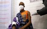 Um homem negro está sentado em uma cadeira e recebe uma vacina em hospital da África