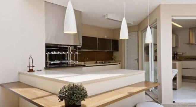 Varanda com churrasqueira pequena branca com balcão de madeira