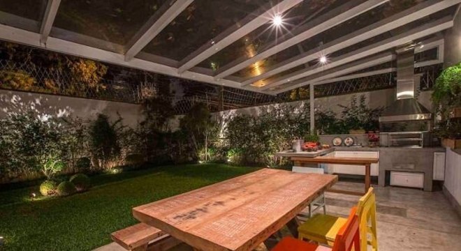Varanda gourmet integrada ao jardim conta com mesa e cadeira de madeira colorida