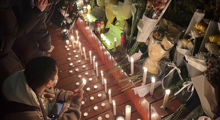 Manifestantes se reúnem ao longo de uma rua com velas e buquês de flores em Pequim