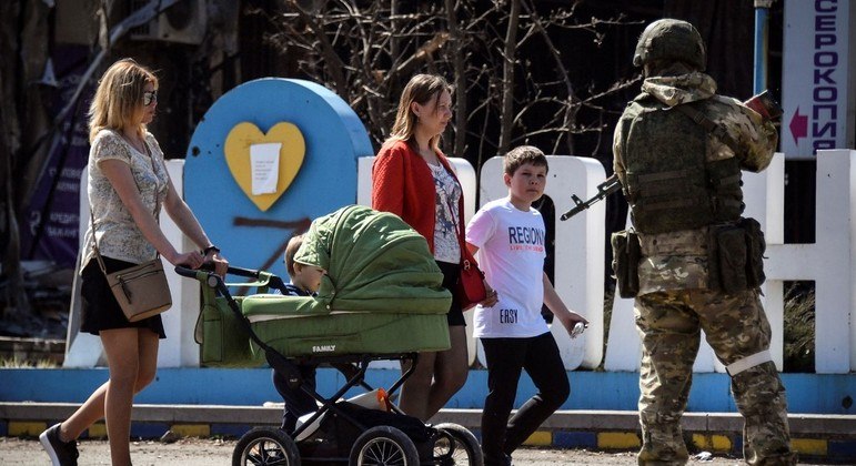 Crianças de Volnovaja voltam à escola, enquanto soldados andam com fuzil pela rua