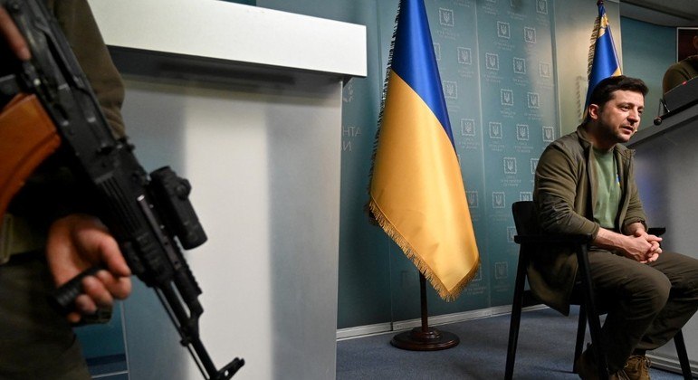 Presidente Volodmir Zelenski é protegido por soldado ucraniano durante entrevista