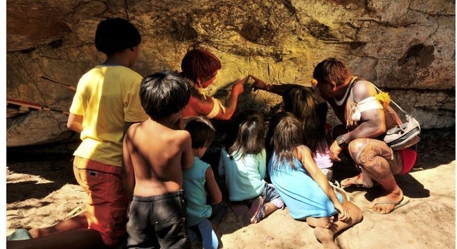 Um índio Waurá ensinando a mitologia em torno do guerreiro Kamukuwaká a crianças da aldeia usando as gravuras da caverna no Xingu antes do local ser vandalizado 