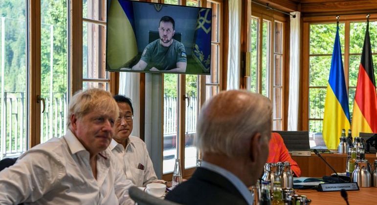 Zelenski (na tela) participa virtualmente da reunião do G7; à esquerda, Boris Johnson, primeiro-ministro do Reino Unido, e, à direita, Joe Biden, presidente dos Estados Unidos